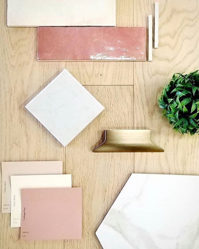 some pink and white tiles are laying on the floor next to a plant with green leaves