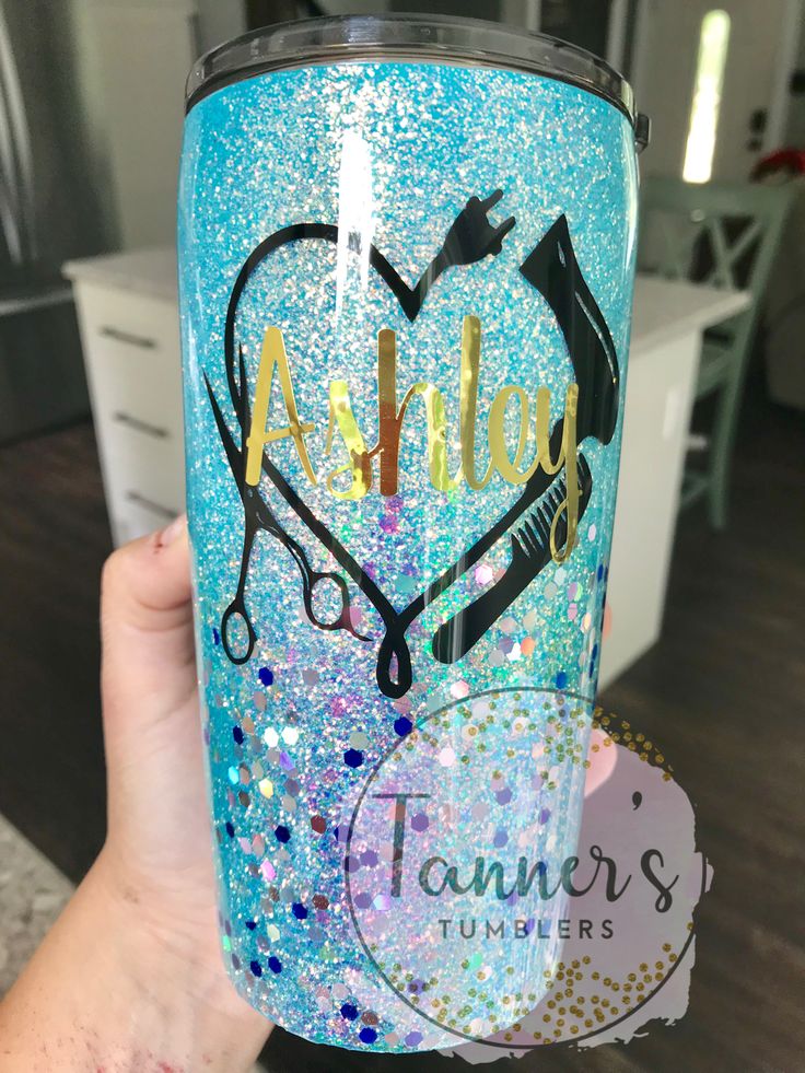 a person holding up a blue glitter tumbler with scissors and heart on the side