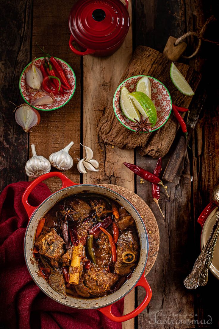 an overhead view of a stew in a red pot on a wooden table with other dishes and utensils