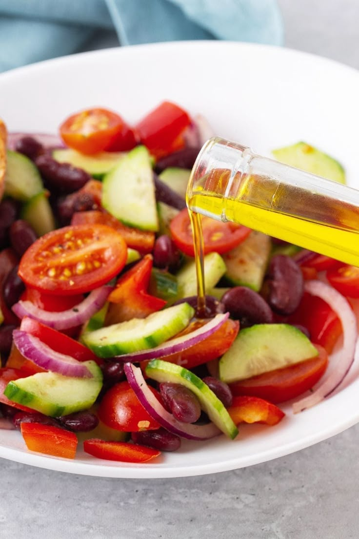 a white bowl filled with cucumbers, tomatoes and onions being drizzled with olive oil