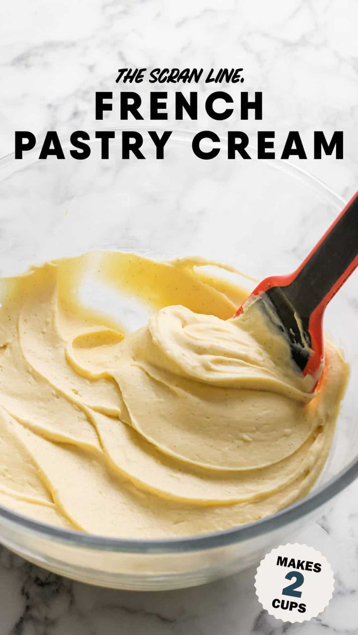 a glass bowl filled with cream on top of a marble counter next to a red spatula