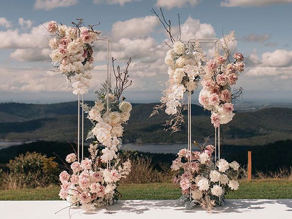 two tall floral arrangements are set up in front of the ocean and mountains for an outdoor ceremony