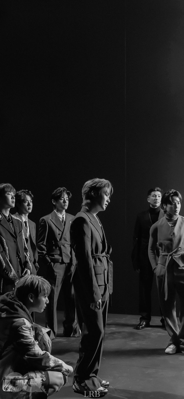 black and white photograph of people standing in front of a dark background with one person sitting on the floor