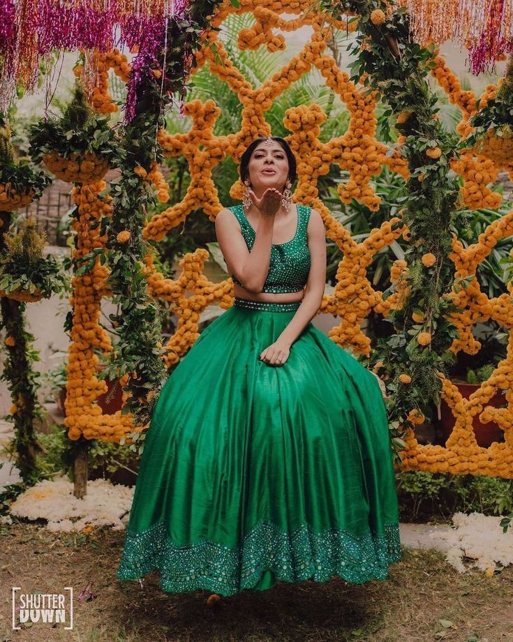 a woman in a green dress is sitting on a bench surrounded by orange and yellow flowers