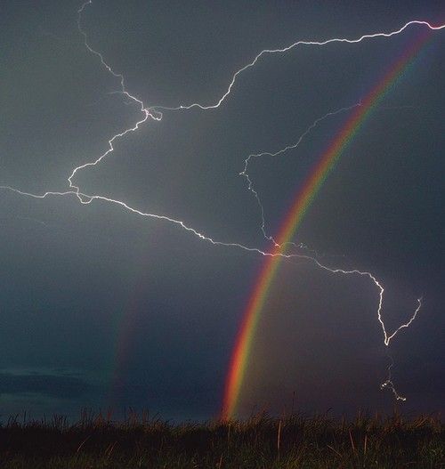 a rainbow appears to be in the middle of a dark sky with clouds and lightning