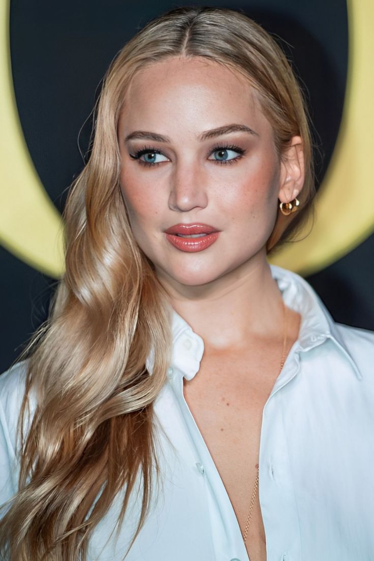 a woman with long blonde hair and blue eyes wearing a white shirt is looking at the camera