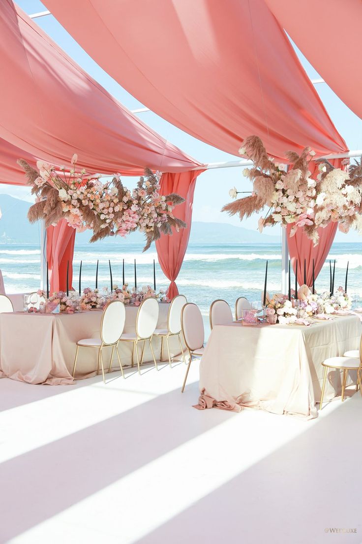 an outdoor wedding setup with pink draping and white linens on the beach