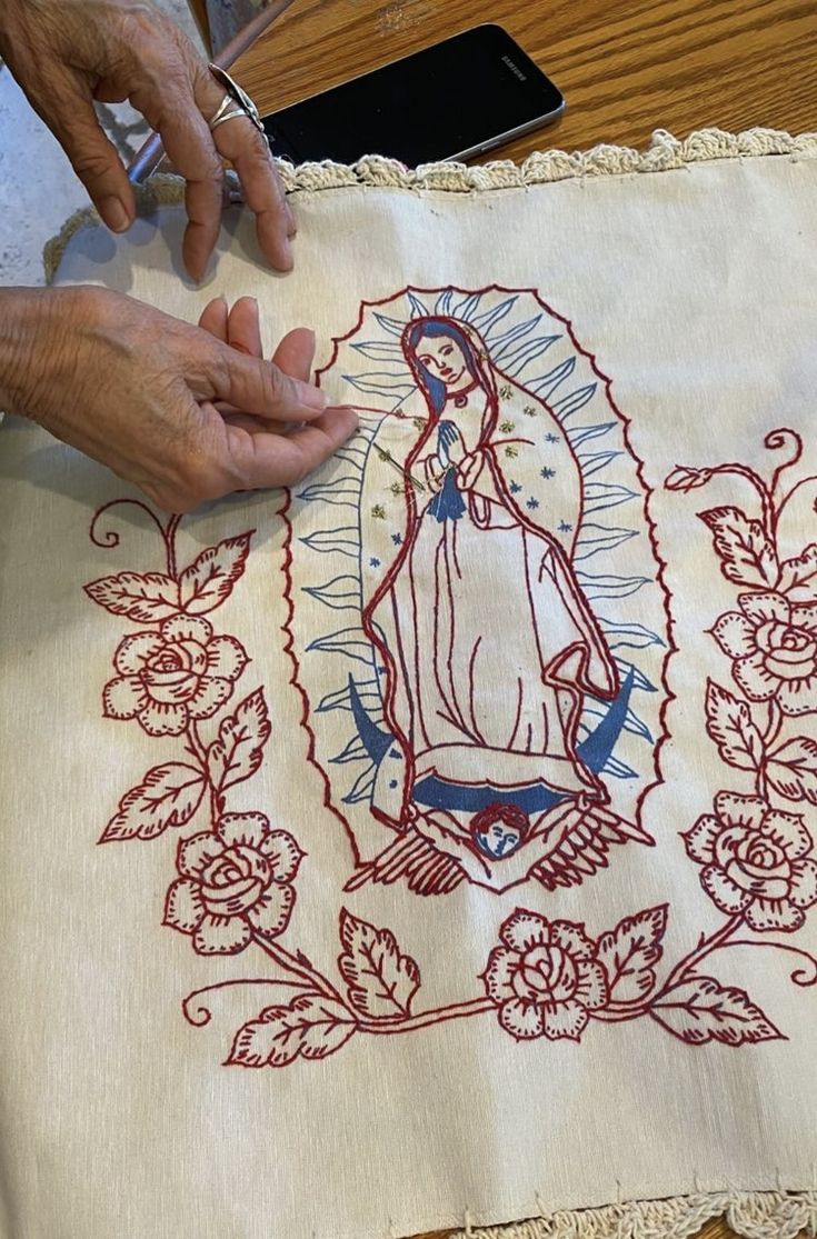 a woman is working on an embroidered cloth with the image of virgin mary in red