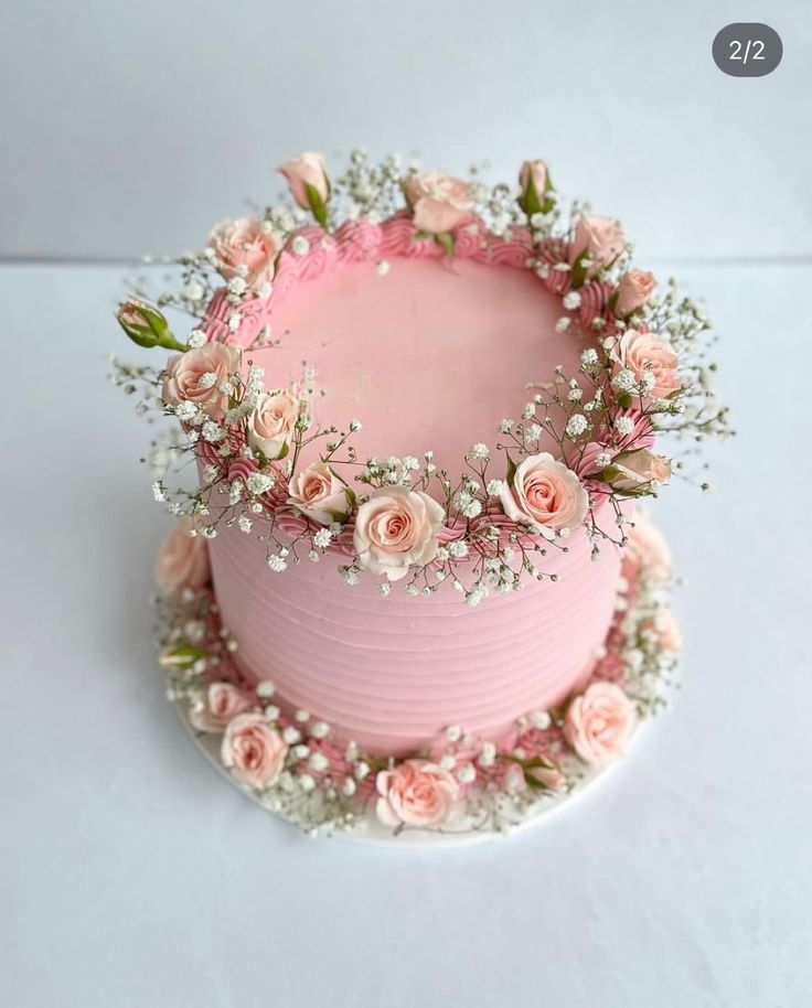 a pink cake decorated with flowers and baby's breath is on a white table