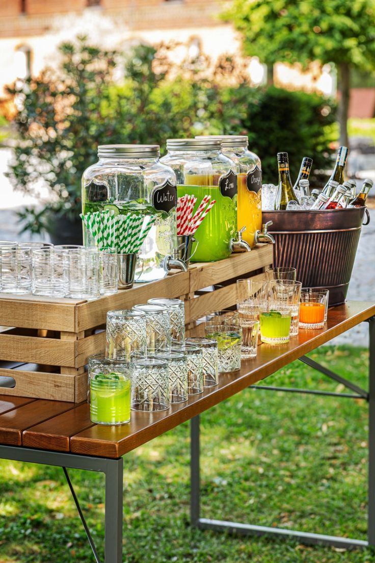 a table with glasses and drinks on it in front of some bushes, grass and trees