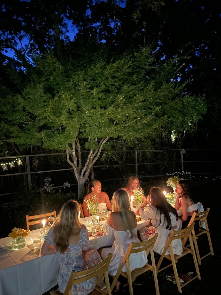 a group of people sitting around a table with candles in their hands at night time