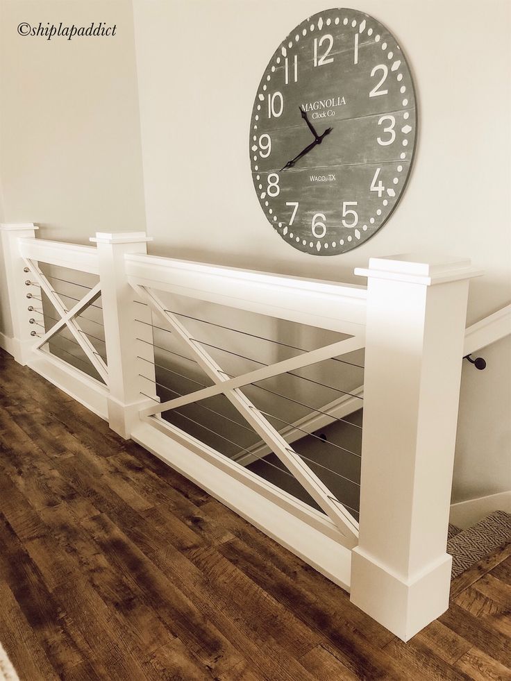 a clock mounted to the side of a wall next to a wooden floor and white railing