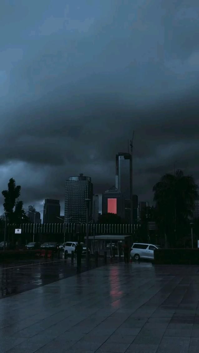 dark clouds loom over the city skyline at night, with cars parked in the foreground