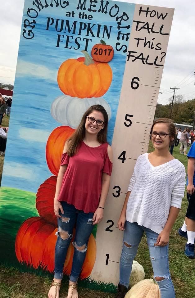 two girls standing next to a tall growth chart with pumpkins painted on the side