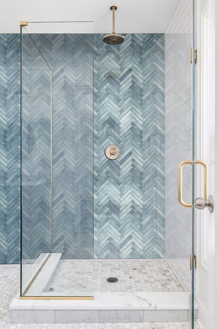 a walk in shower sitting next to a glass door and tiled walls with gold accents