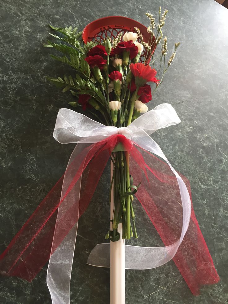 a bouquet of flowers tied to a white pole with a red ribbon on it, sitting on a table