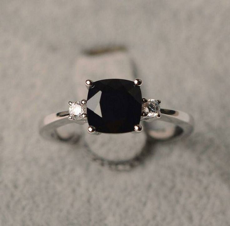 an engagement ring with a black diamond and three diamonds on the side, set in 18k white gold