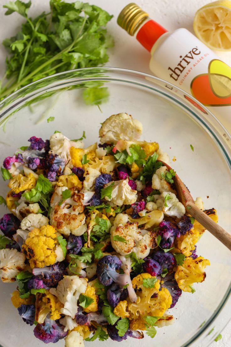 a glass bowl filled with cauliflower, carrots and cilantro next to a bottle of lime juice