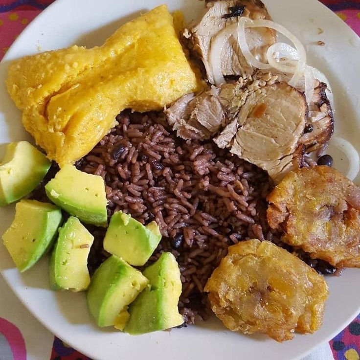 a white plate topped with meat, rice and veggies next to sliced avocado