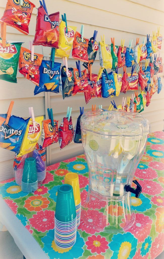 a table topped with lots of candy bags and cups next to a wall filled with candies