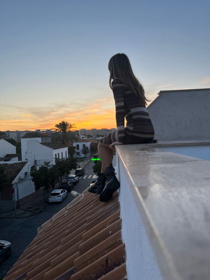 a woman sitting on top of a roof next to a building and looking at the sky