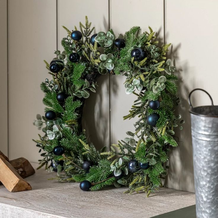 a christmas wreath on a mantle next to a metal bucket