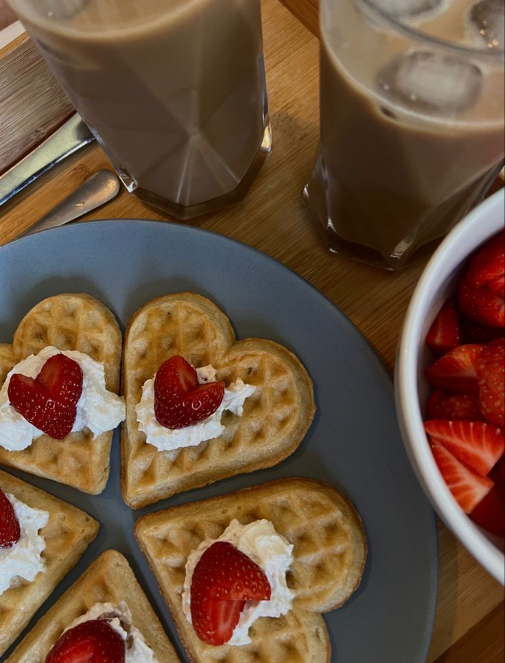 heart shaped waffles with whipped cream and strawberries on a plate next to a glass of milk