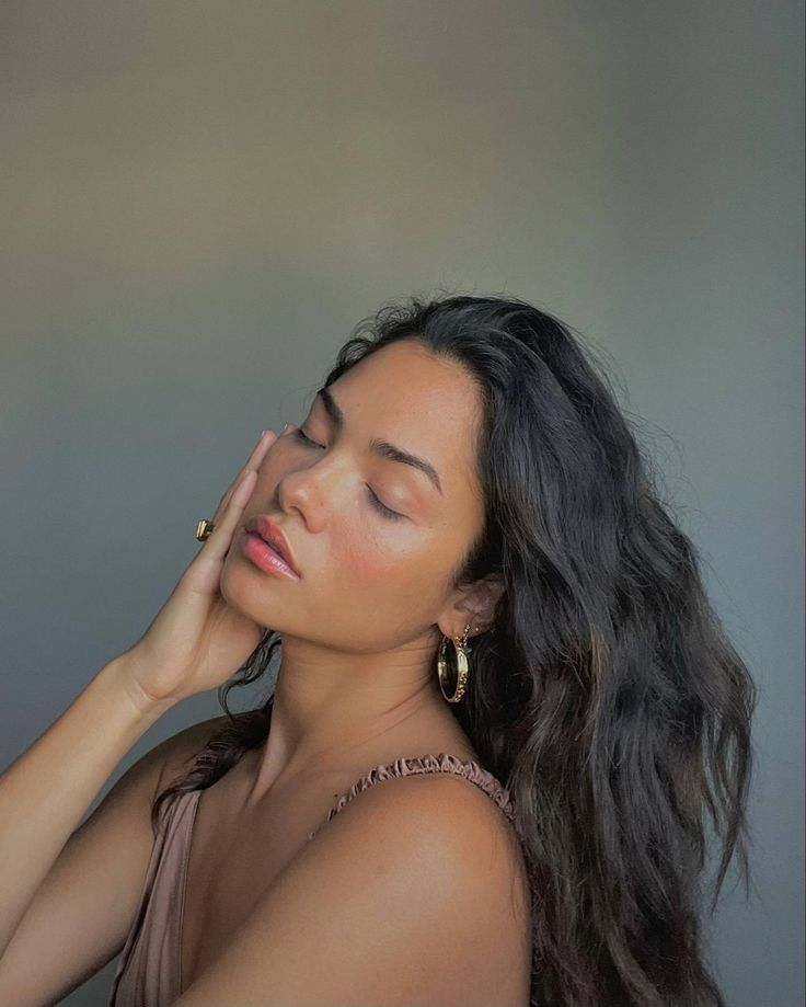 a woman with her eyes closed and hands on her head, leaning against a wall