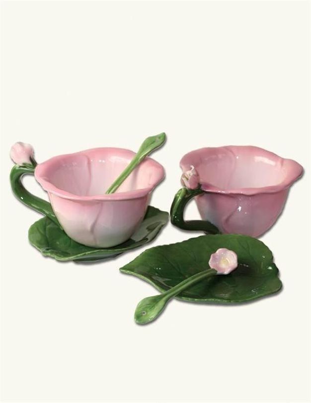 two pink glass cups and saucers sitting on top of green leafy leaves with flowers