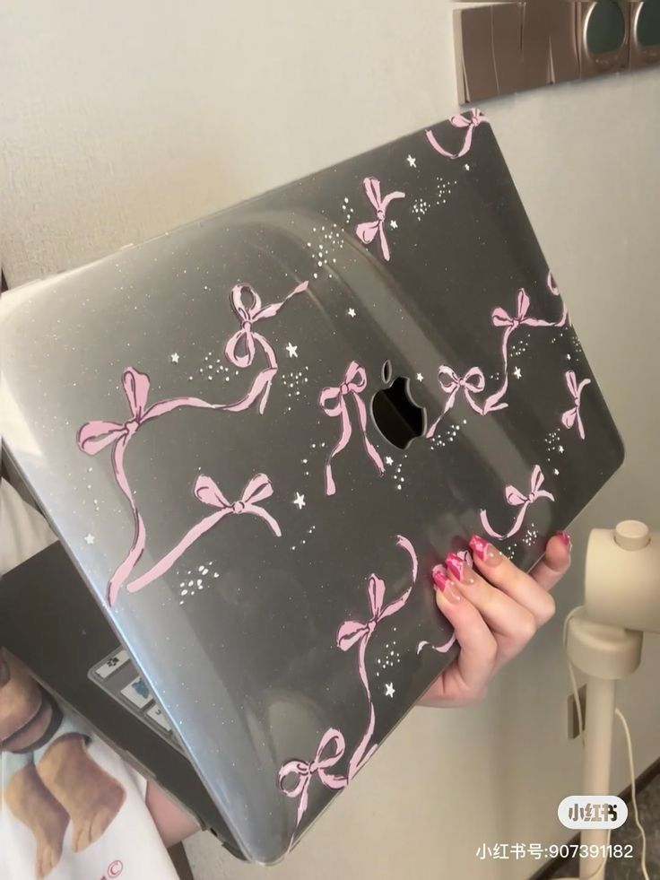 a woman holding an apple laptop with pink bows on it