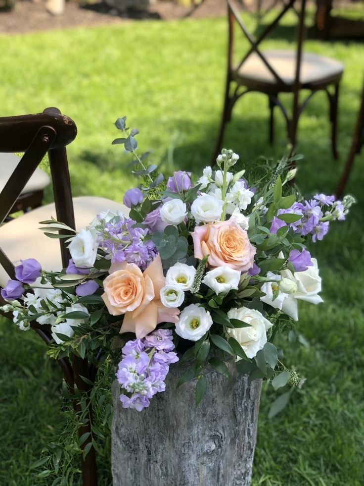 a bouquet of flowers sitting on top of a wooden stump next to chairs in the grass