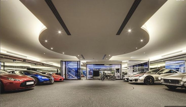 there are many cars parked in this large garage with lights on the ceiling and doors open