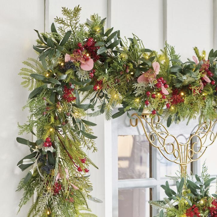 two christmas wreaths hanging from the side of a white building with lights on them