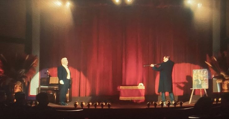 two men standing on stage in front of red curtains