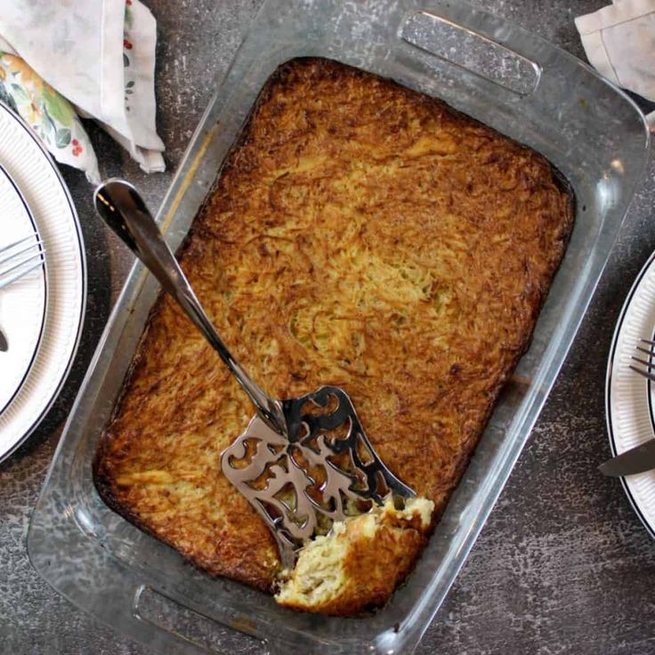 a casserole dish with a spatula in it next to plates and utensils