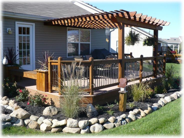 a wooden deck in front of a house with rocks and plants on the ground next to it