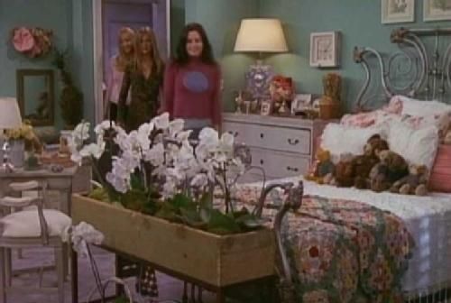 two women standing in a bedroom next to a table with flowers and teddy bears on it