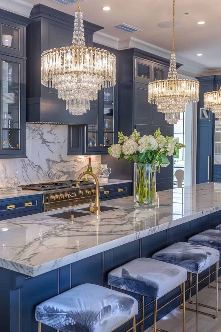 a large kitchen with blue cabinets and marble counter tops, chandeliers hanging from the ceiling