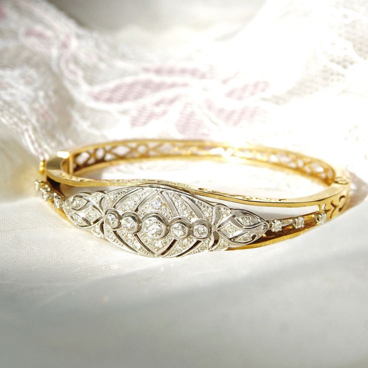 An astounding Edwardian era diamond cluster hinge bangle bracelet in 14k yellow gold and platinum. Features an ornate diamond-encrusted platinum navette setting mounted on a tapered gold band with cutout embellishments and a latch box clasp. Built into the focal point of this bracelet is 5 round-cut diamonds secured in a horizontal line of bezel settings. The open work on either side of the platinum setting is also decorated with three prong-set diamond accents. All the diamonds seem to be in go Antique Round Cuff Bracelet For Wedding, Wedding Bangle In Yellow Gold With Brilliant Cut, Wedding Brilliant Cut Yellow Gold Bangle, Wedding Yellow Gold Bangle With Brilliant Cut, Antique 14k Gold Bangle For Anniversary, Formal Diamond Cuff Bracelet Fine Jewelry, Classic Hallmarked Cuff Bracelet For Wedding, Fine Jewelry Anniversary Bracelet With Rose Cut Diamonds, Classic Wedding Bangle Hallmarked