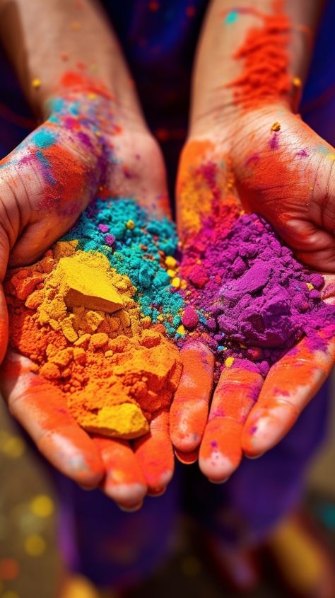 two hands holding colorful powder in the middle of their palms, with colors all over them