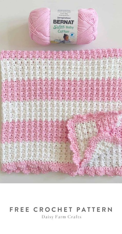 a pink and white crocheted blanket next to a ball of yarn