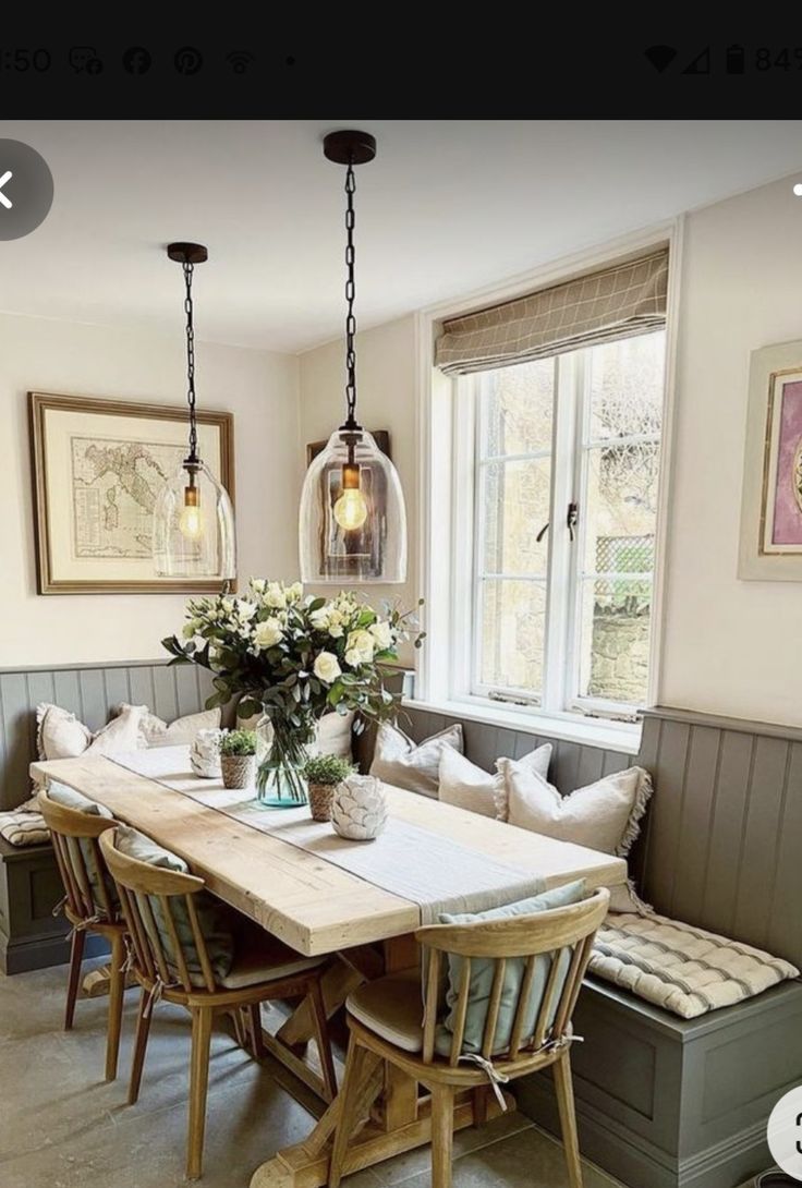 a dining room table and bench with flowers in vases on the top, sitting next to a window