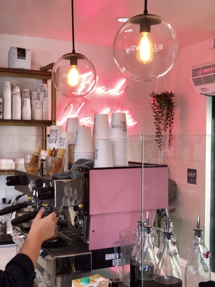 a person is working in a coffee shop with pink walls and hanging lights above the counter