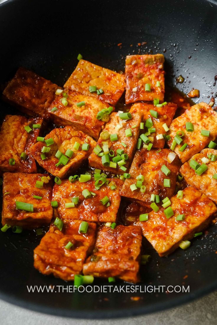 tofu in a skillet with green onions and seasoning on the side, ready to be eaten