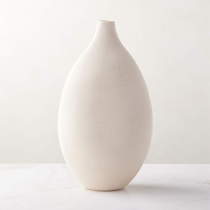 a large white vase sitting on top of a table next to a wall and floor