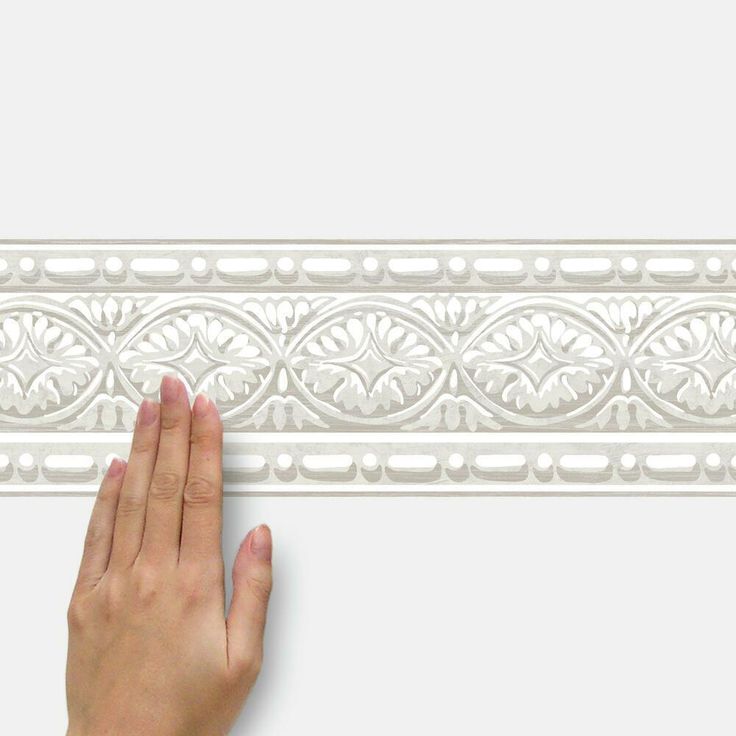 a hand is reaching up to the edge of a decorative molding piece that has been painted white