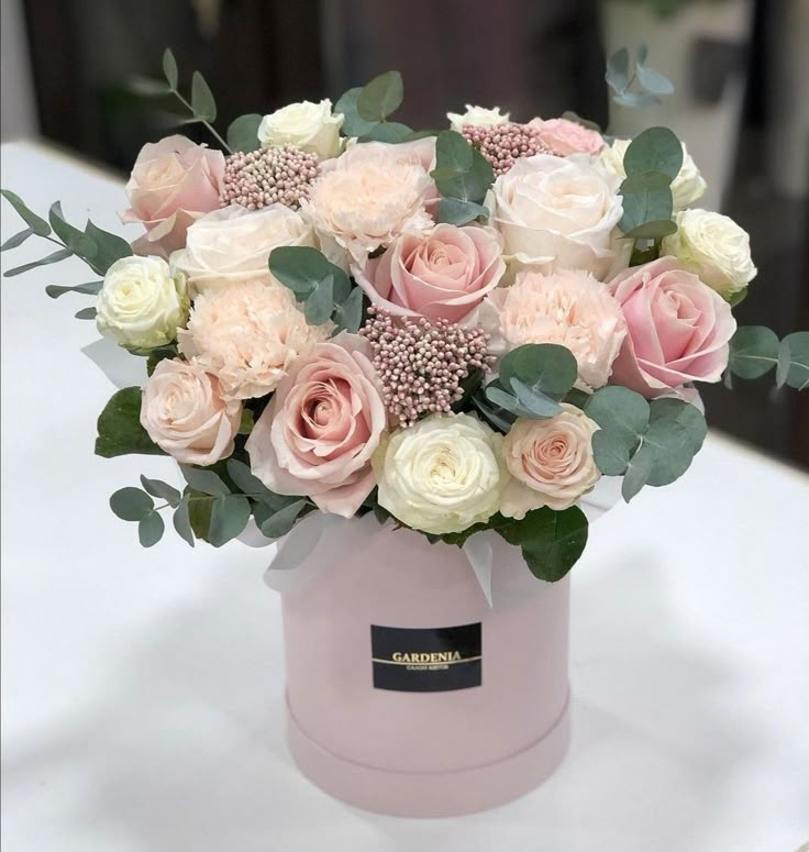 a pink and white flower arrangement in a round vase on a table with greenery