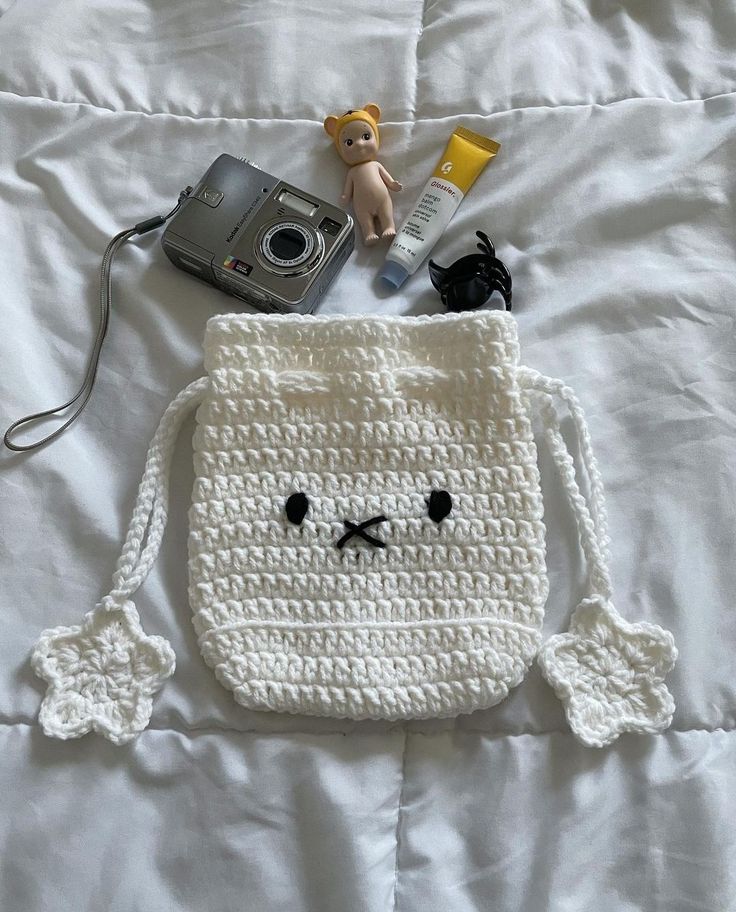 a white crocheted bag with a camera and other items on top of it