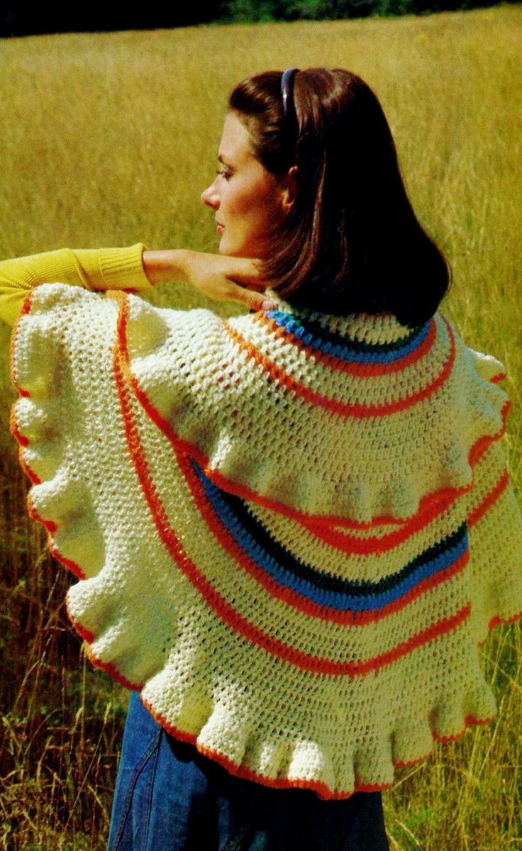 a woman is standing in the grass holding a shawl