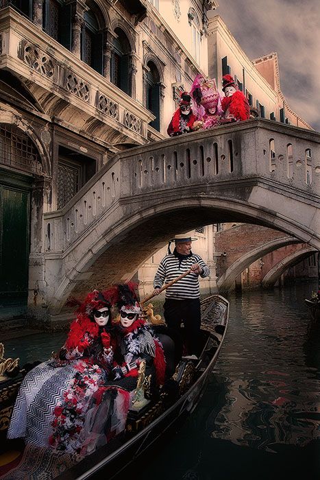 two people in masks are riding on a gondola down the canal under a bridge